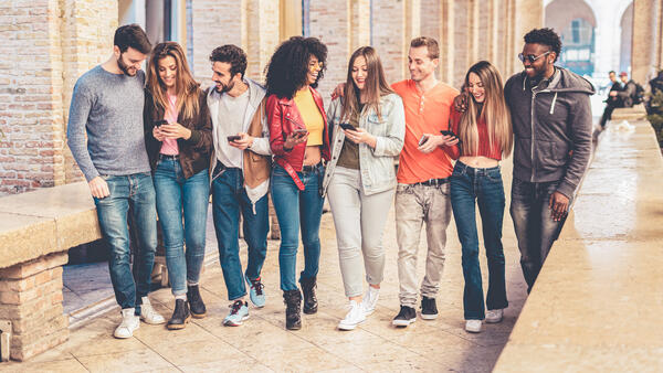Bild vergrößern: Das Bild zeigt eine Gruppe frhlicher junger Menschen die sich im Stadtzentrum treffen. Sie haben Spa mit ihren Smartphones und sozialen Medien, gehen zusammen spazieren und plaudern zusammen.