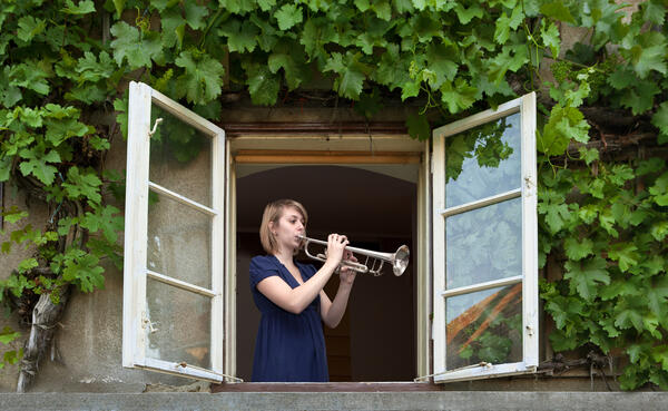 Bild vergrößern: Mädchen spielt am Fenster Trompete.