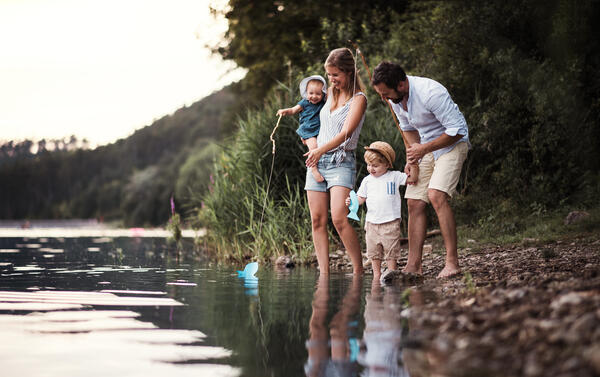 Bild vergrößern: Das Bild zeigt eine junge Familie mit zwei Kindern welche an einem Ufer von eine See stehen. Die beiden Kinder haben eine kleine Angel mit einem Fisch aus Papier daran in der Hand