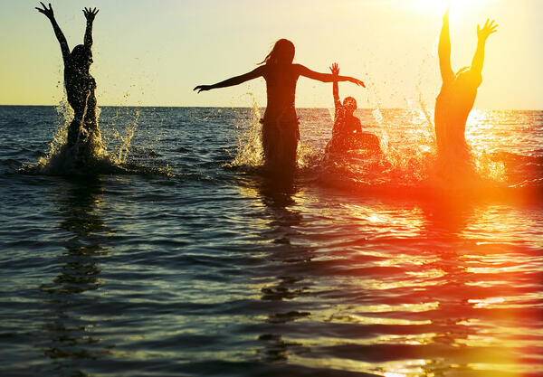 Bild vergrößern: Das Bild zeigt junge Menschen beim Sonnenuntergang im Wasser.