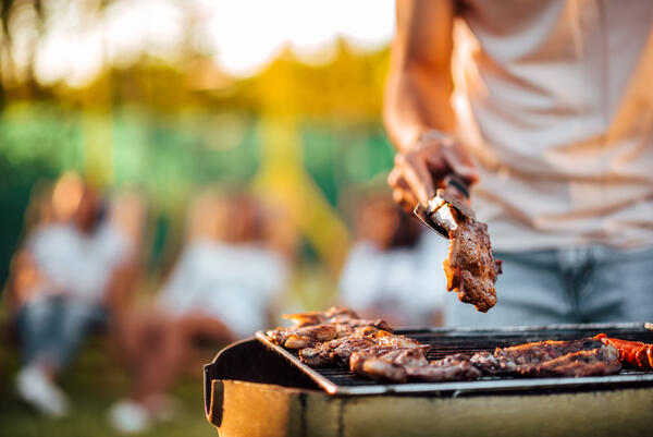 Bild vergrößern: Auf dem Bild wendet eine Person ein saftiges Stück Fleisch auf dem Grill.
