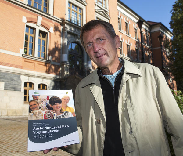 Bild vergrößern: Hartmut Briese hält den Ausbildungskatalog Vogtlandkreis in die Kamera. Dabei steht er vor dem Gymnasium in Oelsnitz.