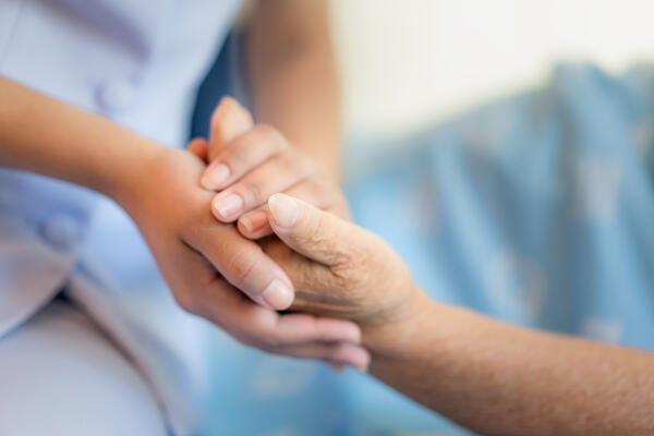 Bild vergrößern: Auf dem Bild hält eine Pflegekraft die Hand einer älteren Frau.