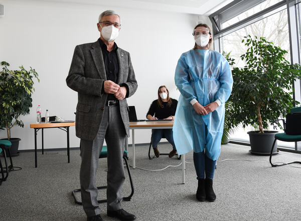 Bild vergrößern: Landrat Rolf Keil steht neben einer Mitarbeiterin aus dem Gesundheitsamt des Vogtlandkreises. Diese trägt zur Testung der Mitarbeiter vogtländischer Unternehmen einen Schutzkittel sowie eine Schutzbrille und Maske.