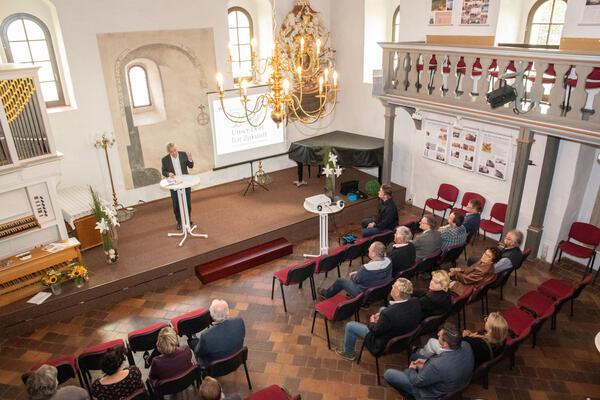 Bild vergrößern: Das Bild zeigt Landrat Rolf Keil auf der Bühne in der Kapelle in Neuensalz. Er hält eine Rede und gibt die diesjährigen Gewinner im Wettbewerb "Unser Dorf hat Zukunft" bekannt.