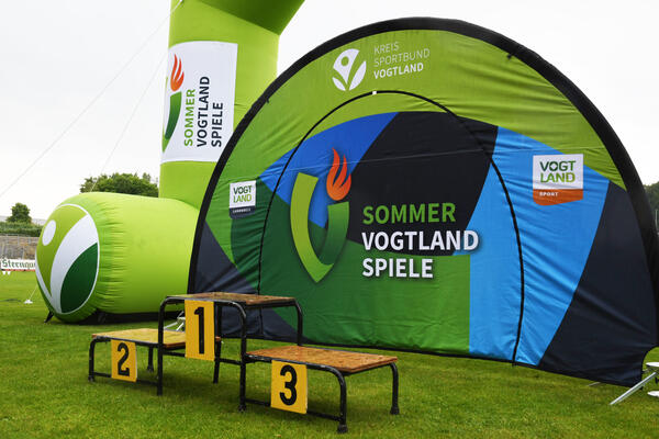 Bild vergrößern: Das Siegertreppchen vor dem grünen Logo der Vogtlandsommerspiele.