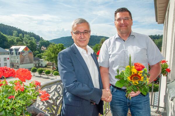 Bild vergrößern: Landrat Rolf Keil und sein Nachfolger Thomas Hennig stehen bei sonnigem Wetter auf dem Balkon und geben sich die Hand. Thomas Hennig hält einen Blumenstrauß.