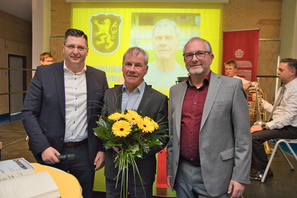 Das Bild zeigt Landrat Thomas Hennig, Volkhardt Kramer, der als "Auerbachs Bürgerpreisträger 2022" ausgezeichnet wurde und den Auerbacher Oberbürgermeister Jens Scharff. Volkhardt Kramer hält einen Blumenstrauß mit gelben Blumen.
