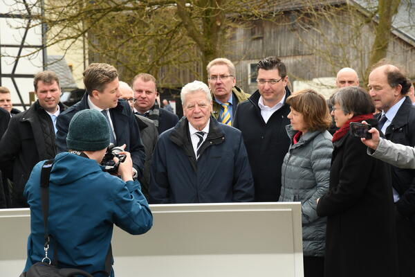 Bild vergrößern: Das Bild zeigt Joachim Gauck und seine Frau Daniela Schadt inmitten einer großen Gruppe von Menschen. Alle stehen vor einer Informationstafel, die an der Gedenkstätte in Mödlareuth zu finden sind.