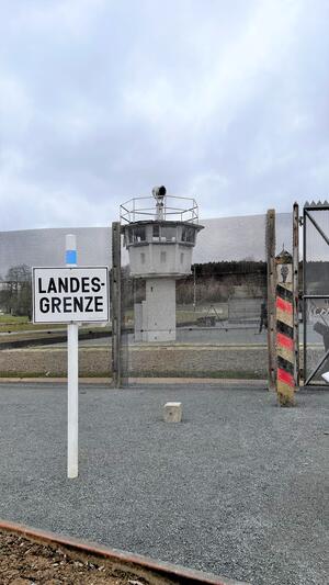 Bild vergrößern: Das Bild zeigt neben einem Schild mit der Aufschrift "Landesgrenze" einen ehemaligen Grenzturm.
