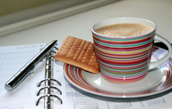 Das Bild zeigt eine Kaffeetasse und einen Terminkalender