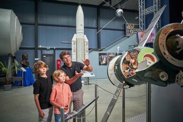 Bild vergrößern: Das Bild zeigt Raumfahrtausstellung in Morgenröthe Rautenkranz. Im Vordergrund ist ein Vater zu sehen, der seinen beiden Söhnen etwas zur Ausstellung erklärt.