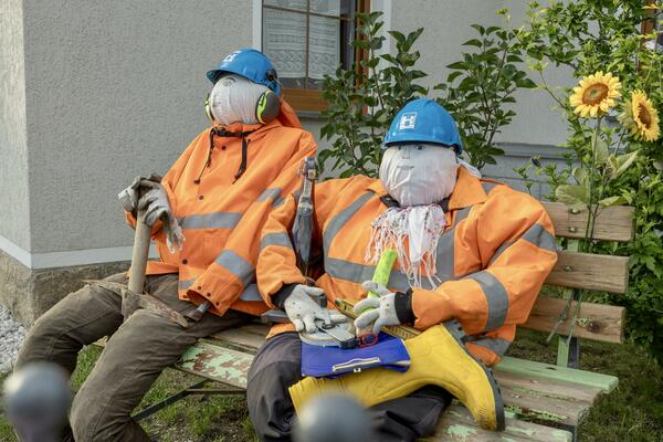 Bild vergr&ouml;&szlig;ern: Stroh-Puppen verkleidet als Bauarbeiter sitzen auf einer Bank.