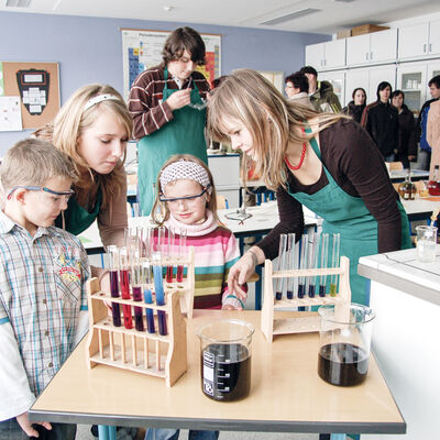 Chemielabor in einer Schule: Lehrerin erklärt Schülern etwas zu den Reagenzgläsern auf dem Tisch.