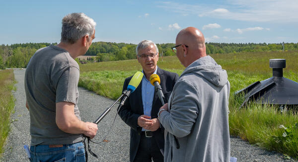 Bild vergrößern: Deponie Zobes: Landrat Rolf Keil im Gespräch mit zwei Rundfunkjournalisten, im Hintergrund die Deponie Zobes.