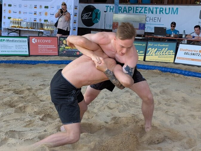 Zwei junge M&auml;nner ringen auf Sand.