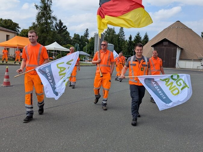 Stra&szlig;enw&auml;rter und -meister halten Vogtlandkreis- und Deutschlandfahnen hoch. Einer tr&auml;gt eine Trommel.