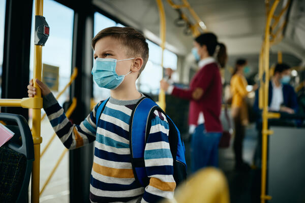 Bild vergrößern: Auf dem Bild sieht man ein Kind in einem öffentlichen Bus mit Mundschutz.