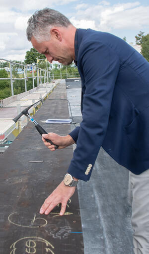 Bild vergrößern: Das Bild zeigt Rettungszweckverbandschef Carsten Michaelis beim Einschlagen des Richtfest-Nagels ins Gebälk.