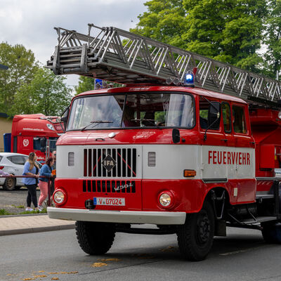 Bild vergr&ouml;&szlig;ern: Historisches rotes Feuerwehrfahrzeug mit Drehleiter f&auml;hrt w&auml;hrend des Festumzugs durch Falkenstein, Zuschauer stehen am Stra&szlig;enrand.