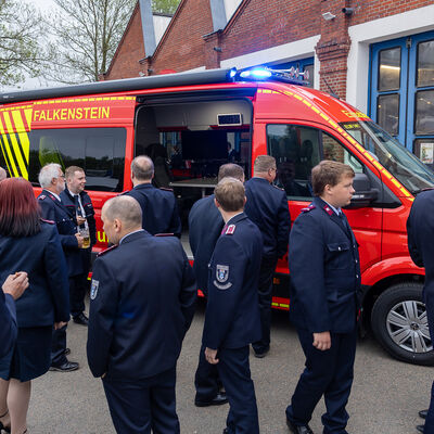 Bild vergr&ouml;&szlig;ern: Roter Einsatzleitwagen der Feuerwehr Falkenstein mit eingeschaltetem Blaulicht vor dem Ger&auml;tehaus, umgeben von Feuerwehrleuten in Uniform.