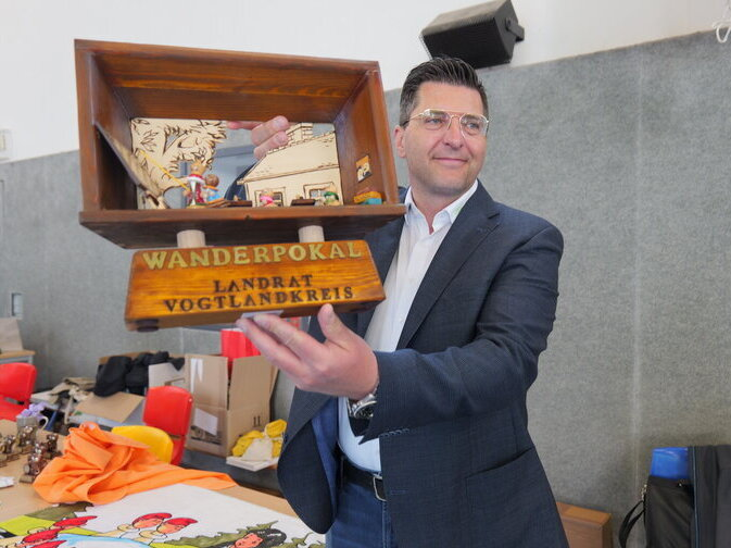 Landrat Thomas Hennig h&auml;lt einen Wanderpokal hoch. Er ist aus Holz gefertigt und zeigt eine Schachklasse.