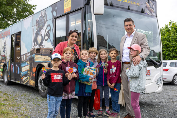 Bild vergr&ouml;&szlig;ern: Eine Gruppe von Grundschulkindern steht gemeinsam mit der Schulleiterin und Landrat Thomas Hennig vor dem Kreisb&uuml;cherbus. Einige Kinder halten selbst gebastelte Blumen und B&uuml;cher in den H&auml;nden.
