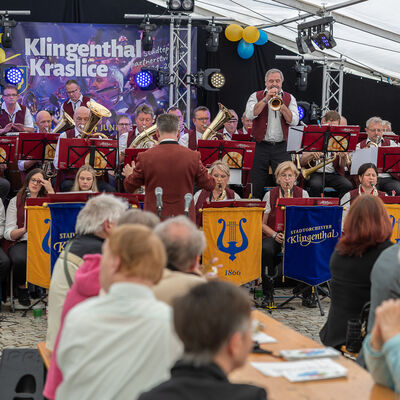 Bild vergr&ouml;&szlig;ern: Ein gro&szlig;es Blasorchester spielt auf einer B&uuml;hne im Festzelt. Im Hintergrund h&auml;ngt ein Banner zum Jubil&auml;um 55 Jahre St&auml;dtepartnerschaft Klingenthal-Kraslice. Vor der B&uuml;hne sitzen zahlreiche G&auml;ste an Biertischen.