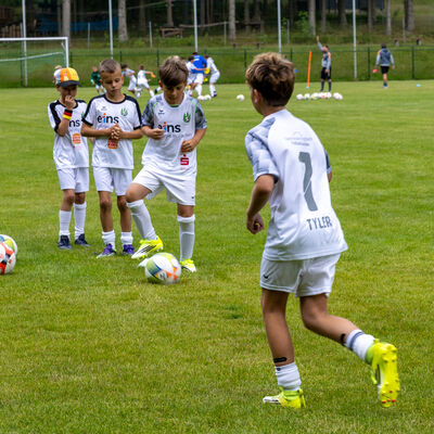 Bild vergr&ouml;&szlig;ern: Kinder trainieren auf einem Rasenplatz. Ein Junge spielt den Ball zu mehreren Mitspielern, im Hintergrund laufen weitere &Uuml;bungen auf dem Fu&szlig;ballfeld.