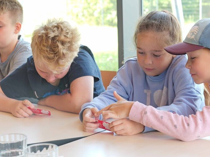 Kinder sitzen an einem Tisch und halten eine kleine Karte mit Sirenensignalen in der Hand.