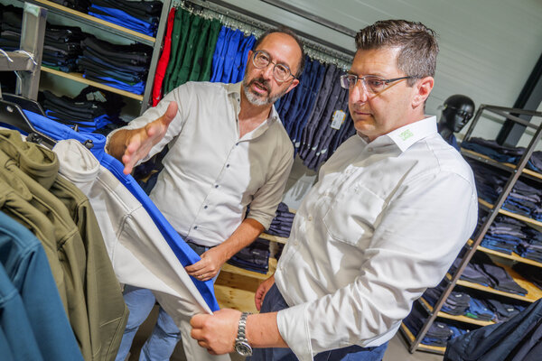 Bild vergr&ouml;&szlig;ern: Das Bild zeigt zwei M&auml;nner beim Ansehen von Arbeitskleidung
