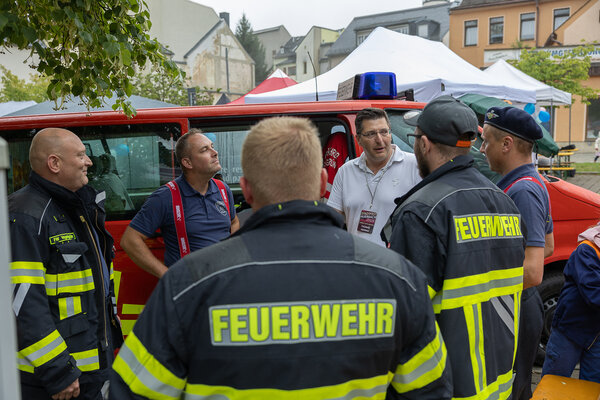 Bild vergr&ouml;&szlig;ern: Landrat Thomas Hennig steht vor einem roten Einsatzfahrzeug und spricht mit mehreren Feuerwehrleuten.
