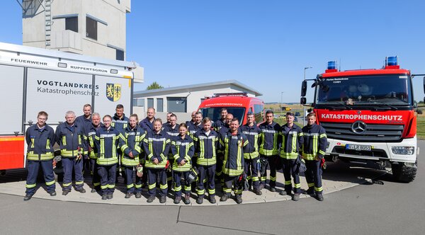 Bild vergr&ouml;&szlig;ern: Das Bild zeigt mehrere Feuerwehrm&auml;nner vor Feuerwehrautos.