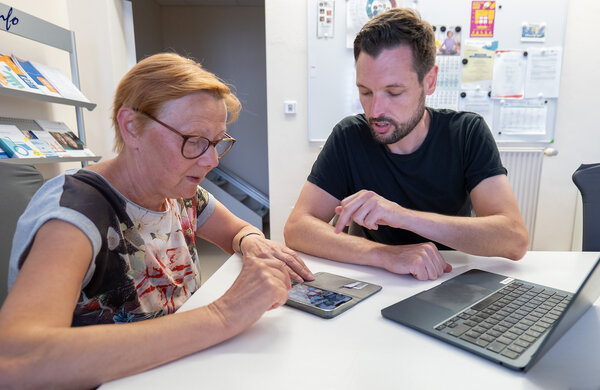 Bild vergr&ouml;&szlig;ern: Zwei Leute sitzen am Tisch und schauen auf Handy
