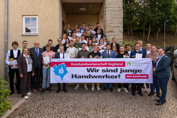 Bild vergr&ouml;&szlig;ern: Gro&szlig;e Gruppe junger Gesellinnen und Gesellen sowie Vertreter der Kreishandwerkerschaft und G&auml;ste vor einem Geb&auml;ude. In der ersten Reihe halten sie ein Banner mit der Aufschrift &raquo;Wir sind junge Handwerker!&laquo;.