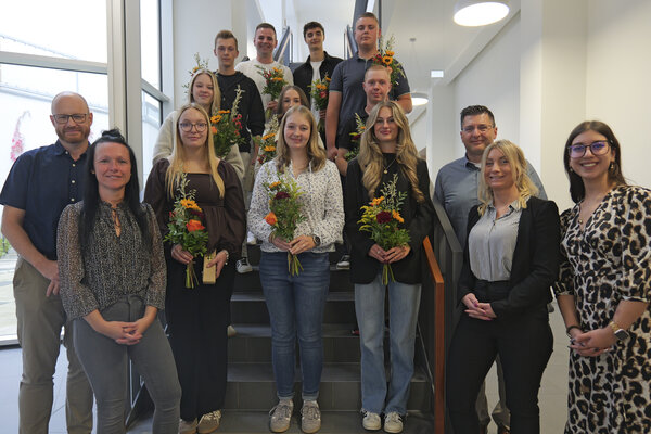 Azubis und Studierende stehen auf einer Treppe und halten Blumen.
