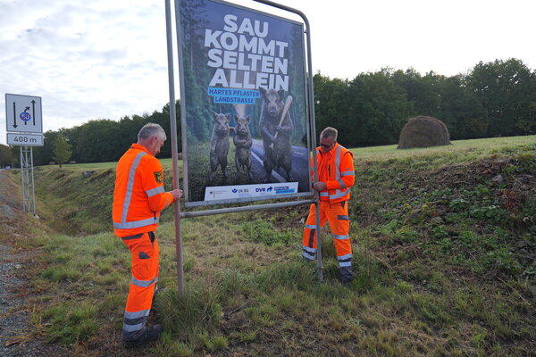 Zwei Mitarbeiter der Stra&szlig;enmeisterei Plauen bringen eine Plakatwand an der B173 an.