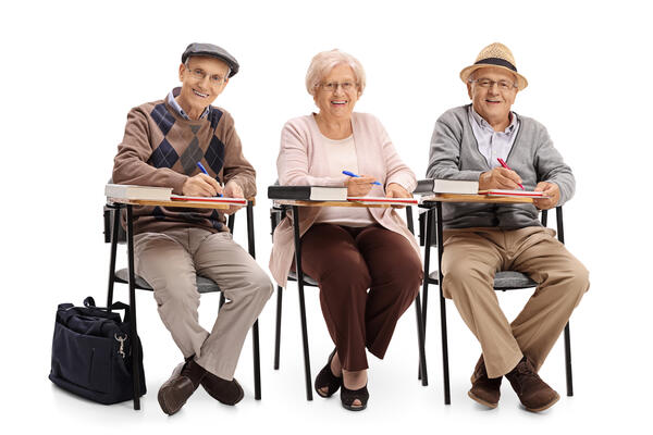 Bild vergrößern: Auf dem Bild sieht man Seniorinnen und Senioren an Schulbänken sitzen.