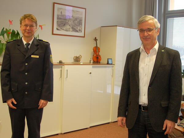 Das Bild zeigt den neuen Polizeipräsidenten Lutz Rodig und Landrat Rolf Keil. Beide stehen im Büro des Landrates und lächeln in die Kamera. Im Hintergrund steht eine Geige auf einer weißen Kommode. 