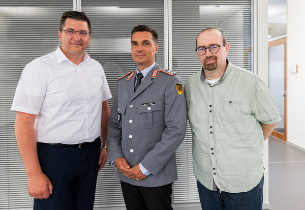 Das Bild zeigt drei M&auml;nner frontal. 